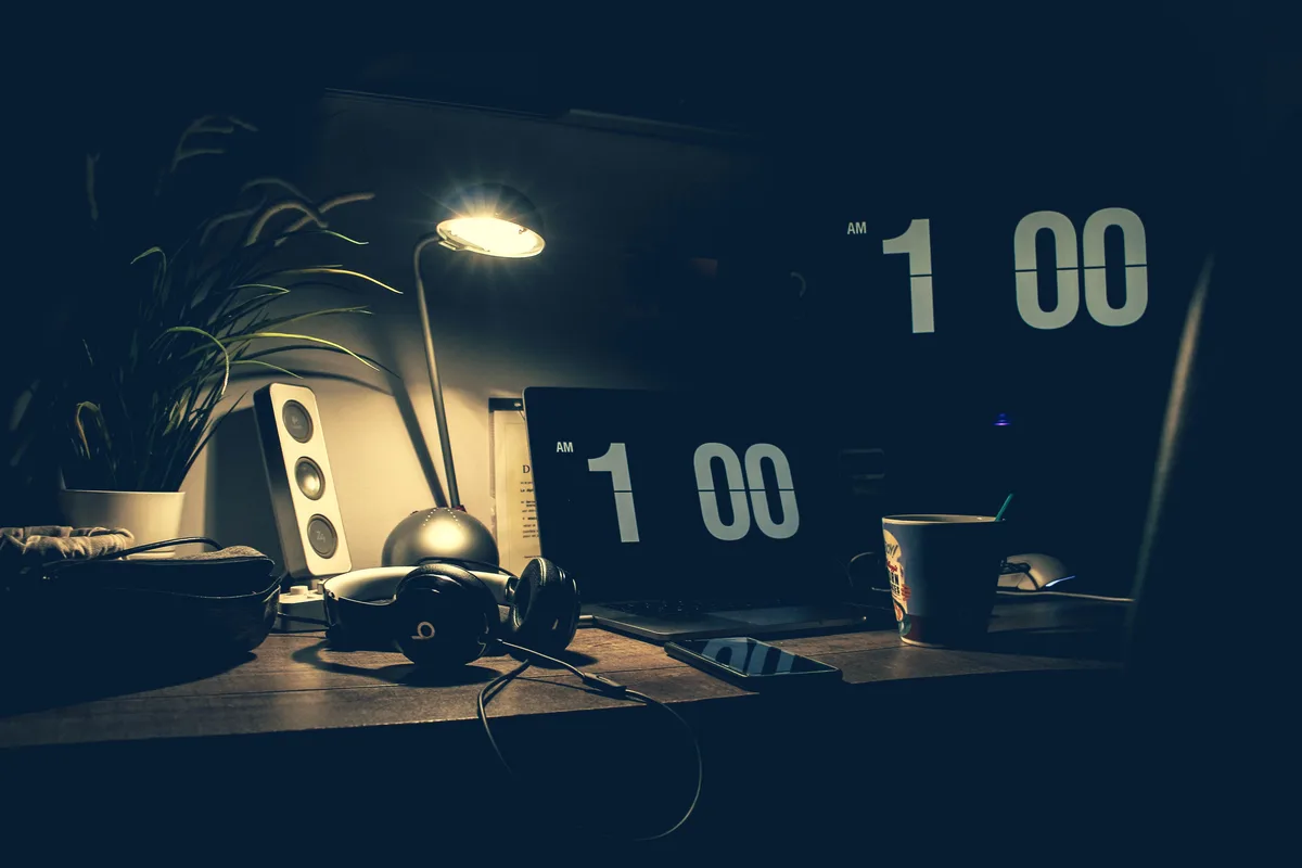A dimly lit desk at 1am with a laptop, headphones, and speakers, representing the late-night work of picking and building a faceless Instagram niche
