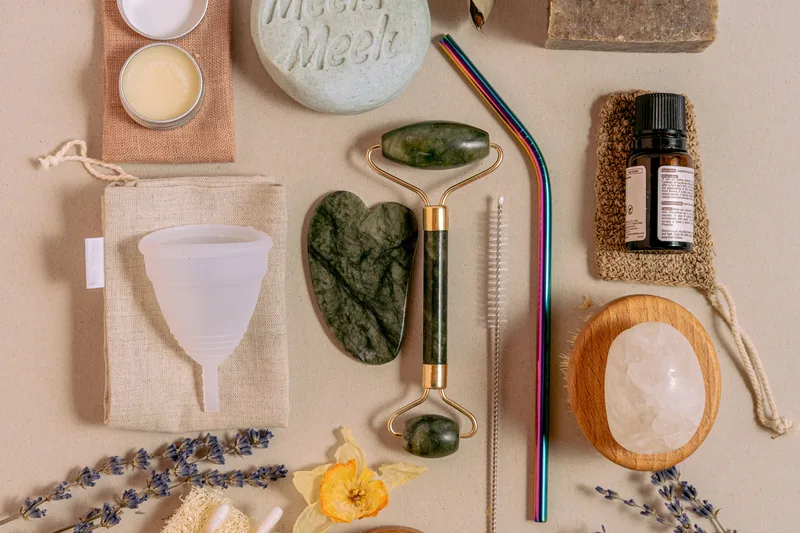 A flat lay of sustainable beauty and lifestyle products, including a reusable jade roller and menstrual cup, representing the faceless sustainable living niche