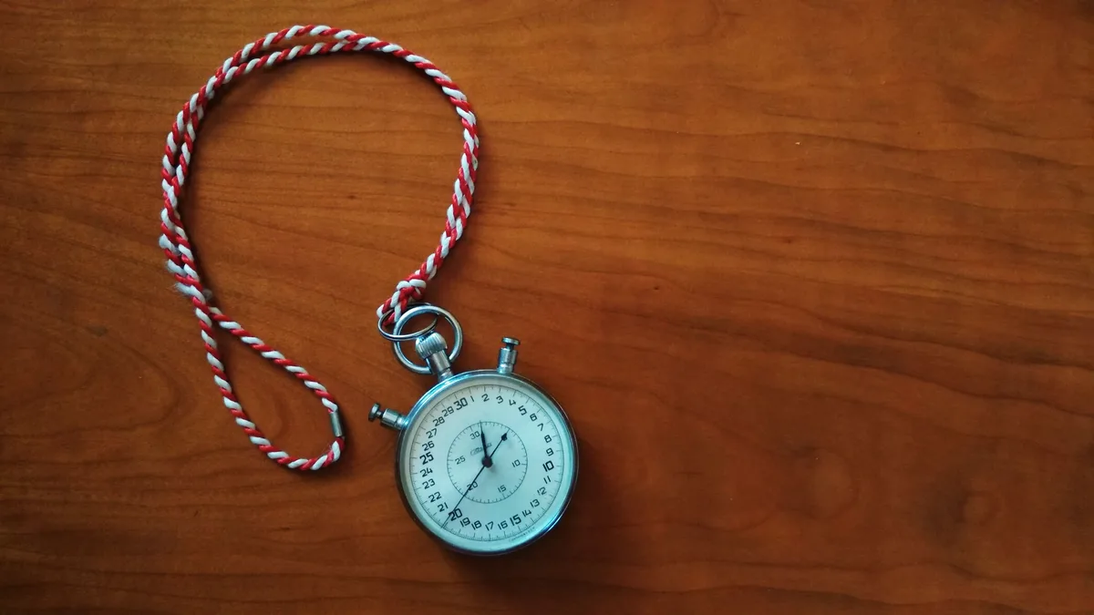 Silver analog stopwatch with a red and white cord on a wooden table