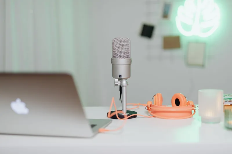 Modern desk setup featuring a condenser microphone, laptop, and headphones in a stylish content creation workspace