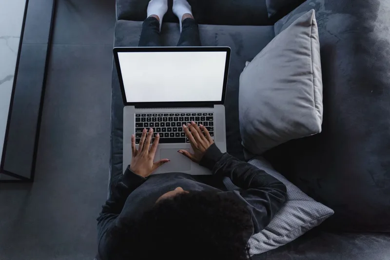 Laptop open on a couch viewed from above, showing a research workflow without revealing the creator&rsquo;s identity