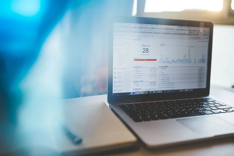 Laptop on a wooden desk displaying a Google Analytics dashboard with traffic data and metrics charts