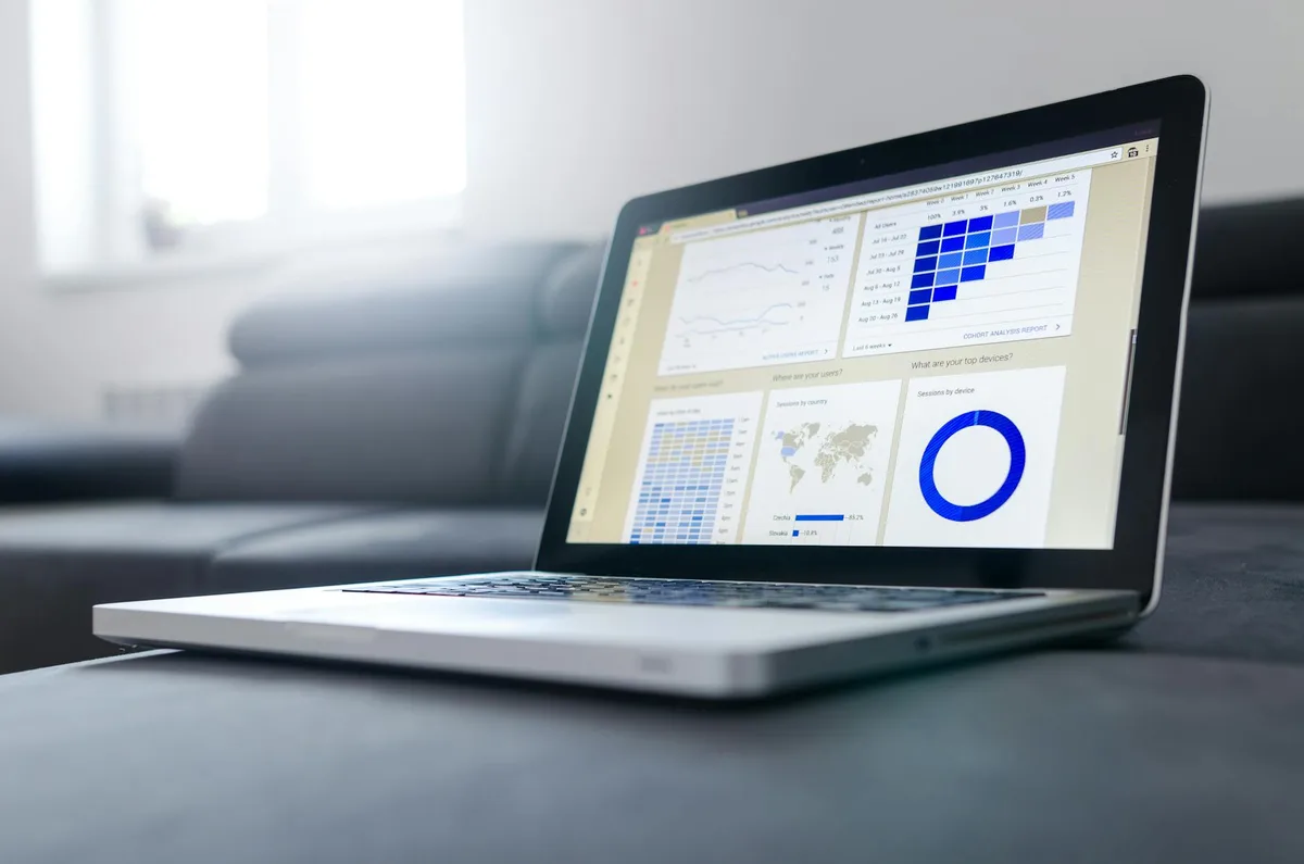 Laptop screen showing a YouTube analytics dashboard with abstract thumbnail grid, dark background with electric teal accents, no human faces