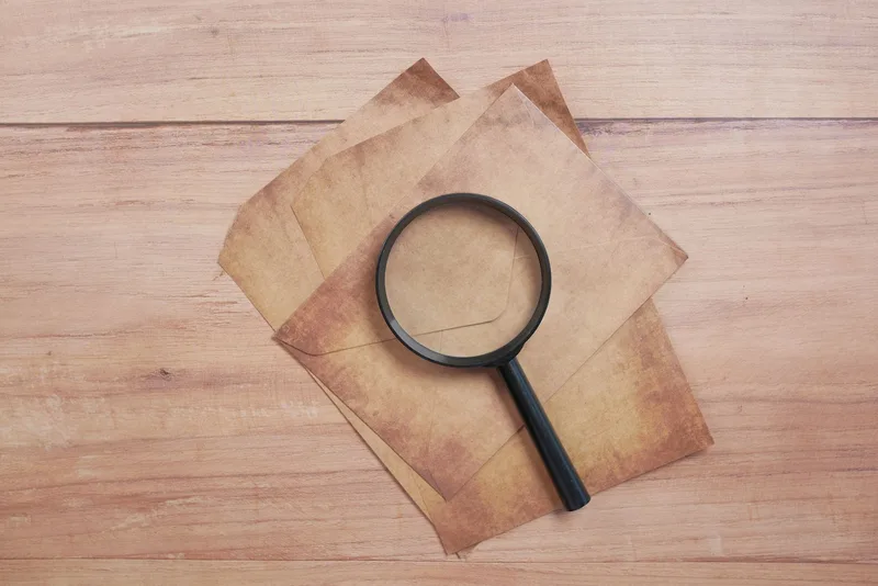 A magnifying glass resting on aged documents, the research-first visual language mystery content relies on