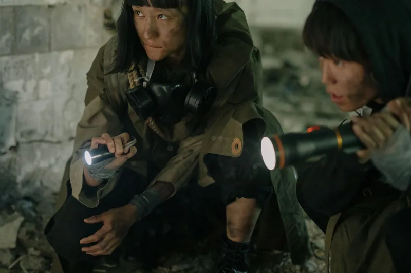 Two figures exploring a dark, decaying urban environment with flashlights