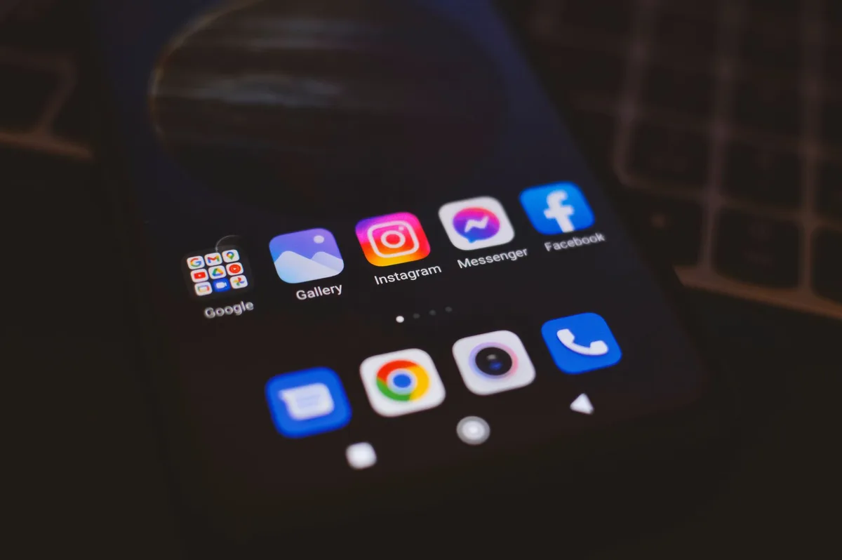Close-up of a phone home screen in a dark room with the Instagram, Messenger, and Facebook app icons in focus