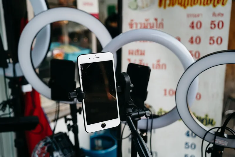 A smartphone clipped to a tripod in front of several ring lights at a street stall