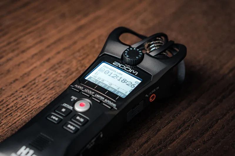 Handheld digital voice recorder with a lit screen and red record button on a wooden table