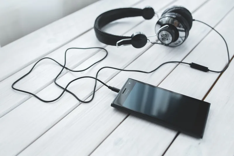 Black smartphone connected to wired headphones on a white wooden desk