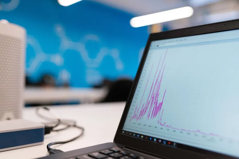 Laptop screen showing a line graph with a sharp decline, next to a desk speaker, in an office setting