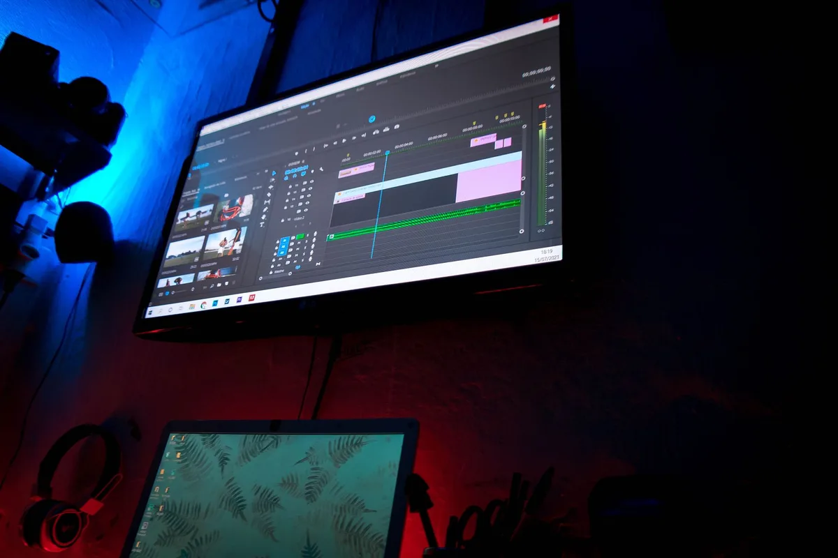 Dark editing room with a wall monitor showing a video editing timeline, lit in blue and red, no person visible