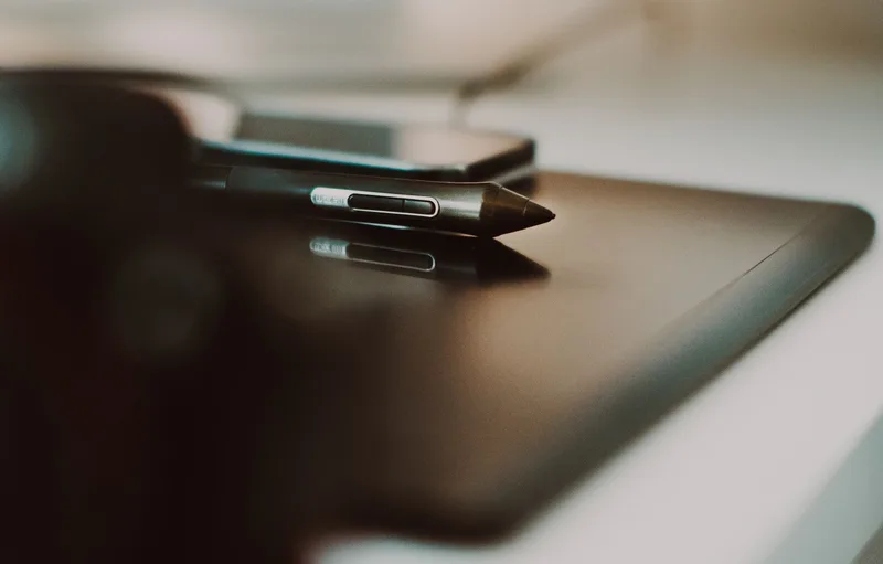 Stylus resting on a black graphics tablet next to a smartphone on a white desk