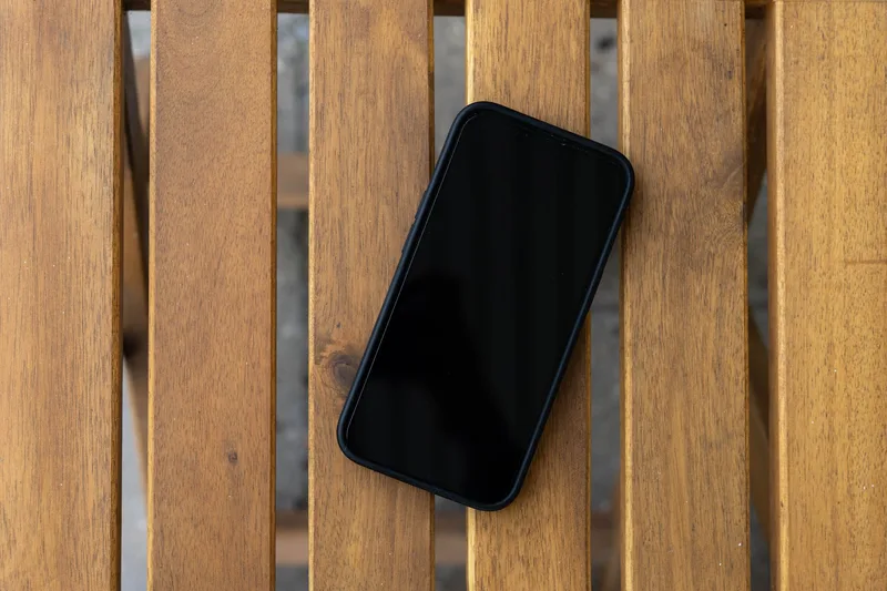 Smartphone with a dark screen lying on a slatted wooden table, viewed from above