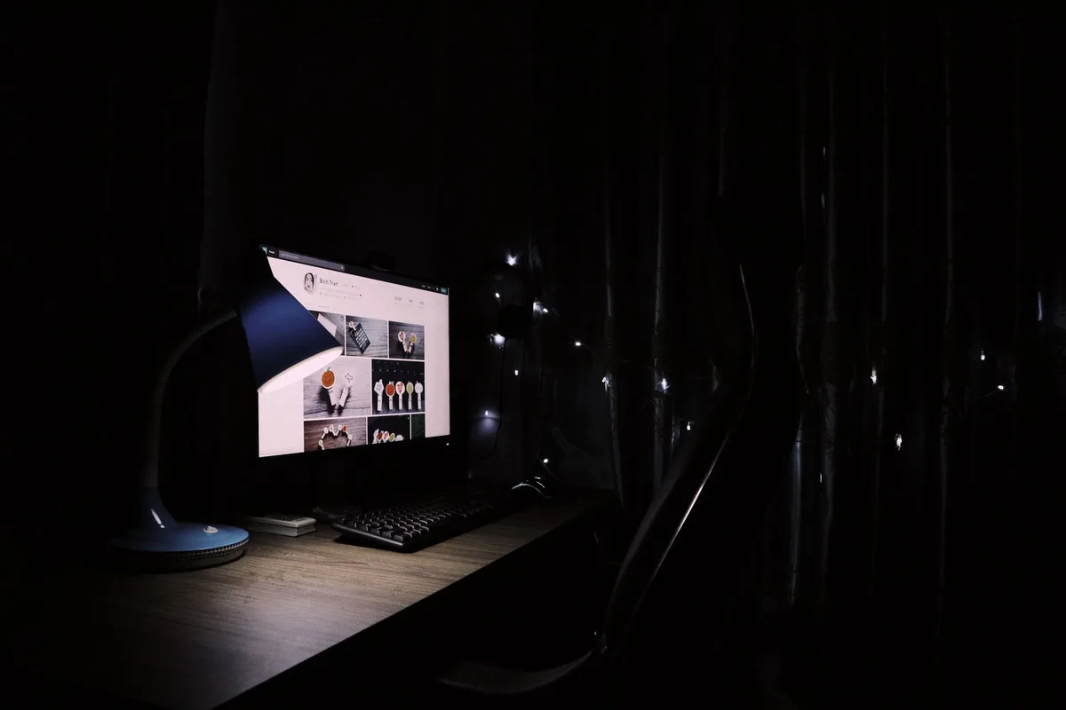 A dimly lit home office desk with a glowing computer monitor, no person visible