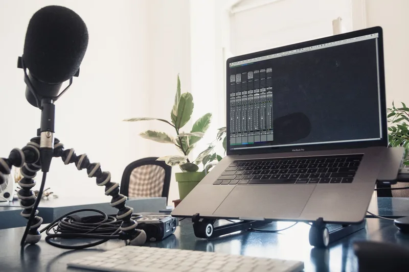 Microphone on a flexible tripod beside a laptop showing an audio mixer, set up for voiceover recording