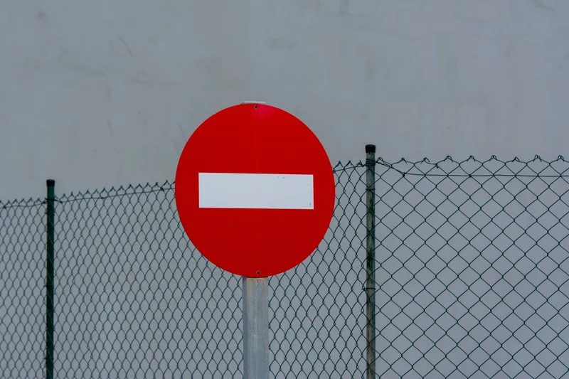 A red circular no-entry sign mounted on a mesh fence, symbolizing an ineligible or rejected status