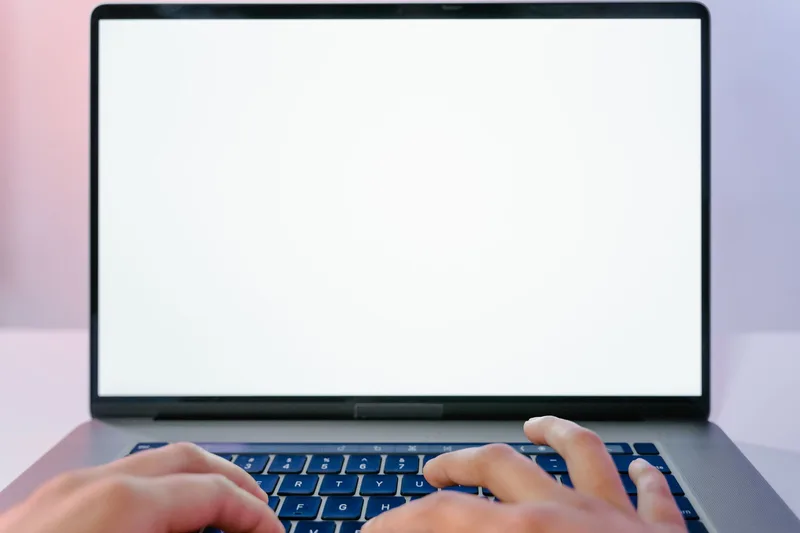 Blank white laptop screen close-up, hands resting on the keyboard, no face visible