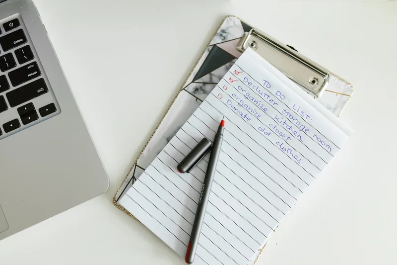 Checklist on a clipboard next to a laptop keyboard, top-down view, no person visible