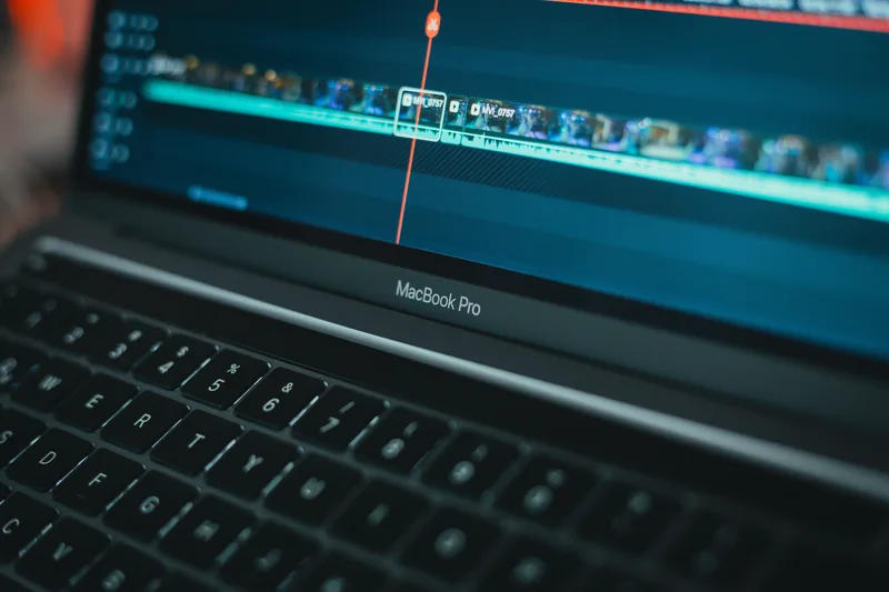 MacBook Pro screen showing a video editing timeline with a red playhead, keyboard in the foreground, no person visible